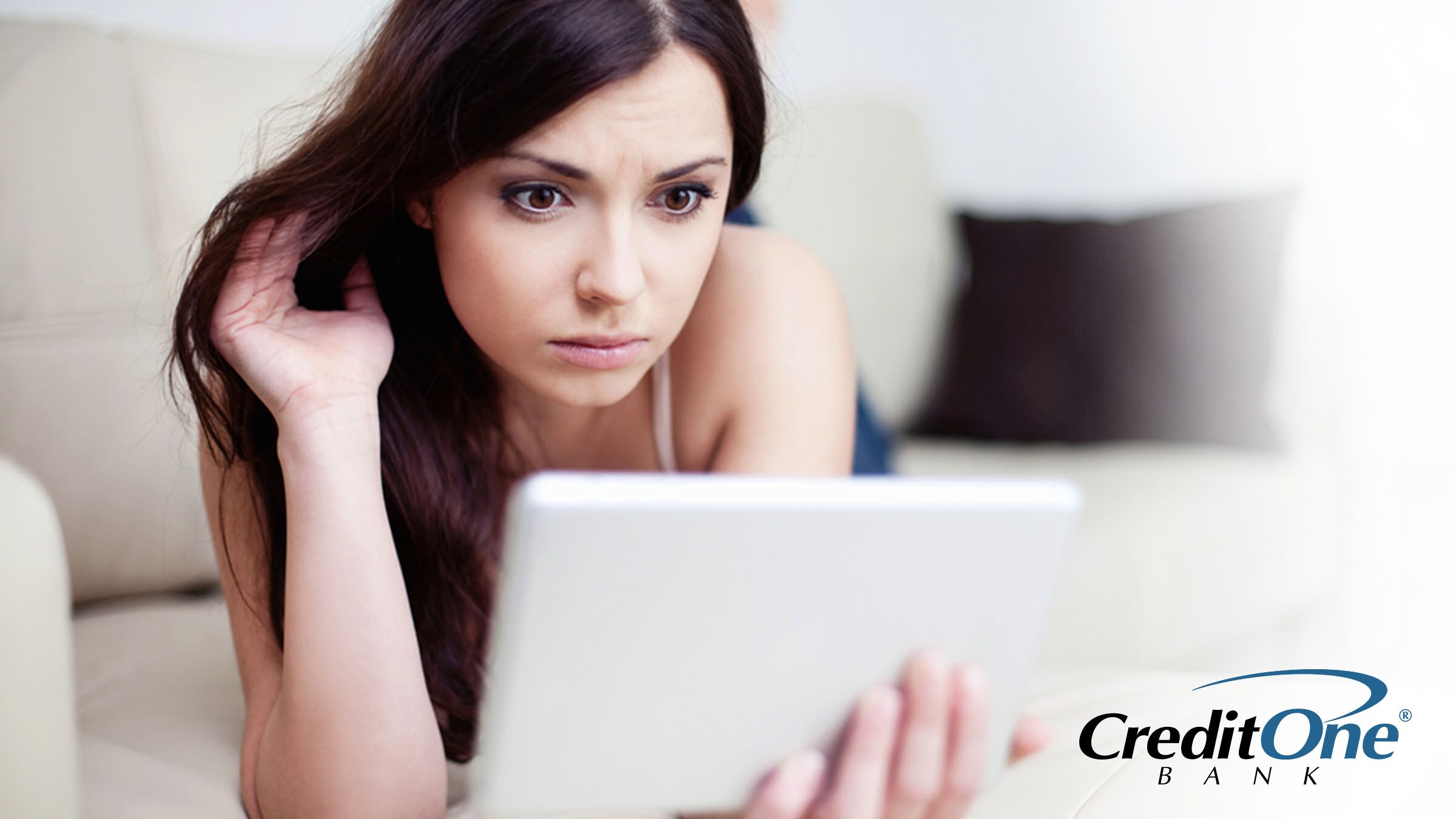 A woman lies on her sofa while reading from a tablet. She may be learning the differences between credit scores, reports and reporting agencies.